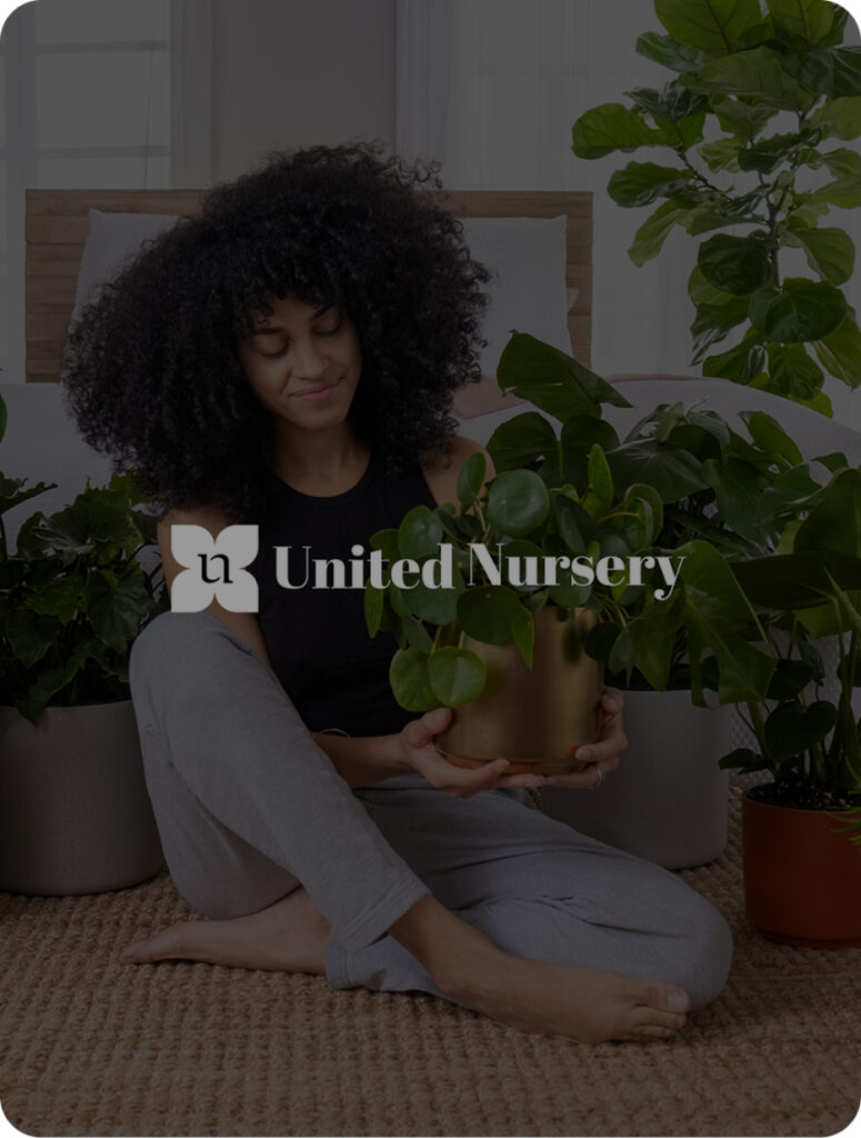 Happy woman holding a plant around a variety of other plants